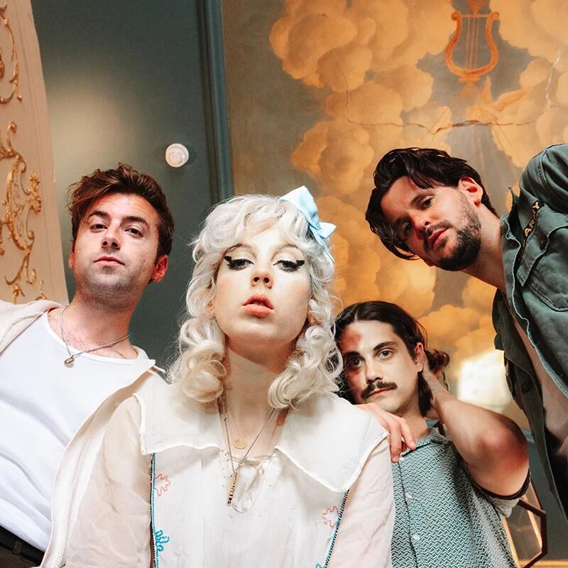 Cztery twarze ludzi w średnim wieku (jedna kobieta w blond włosach) pochylają się nad obiektywem aparatu