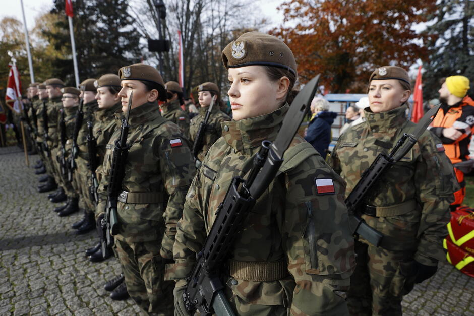 women in uniforms armed with rifles stand guard