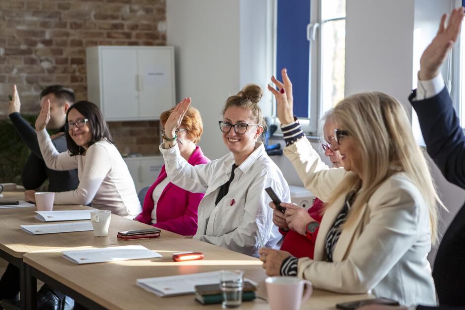 na zdjęciu widać pięć kobiet w średnim wieku, siedzą za stołem, podnoszą rękę głosując, są elegancko ubrane