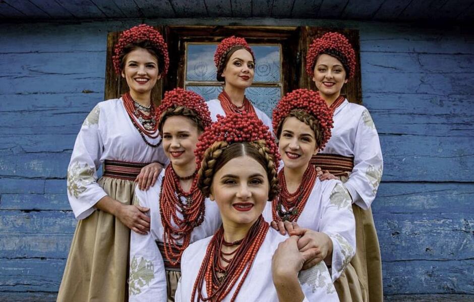 kilka młodych kobiet ubranych w stroje ludowe, stojących na tle starej wiejskiej chaty