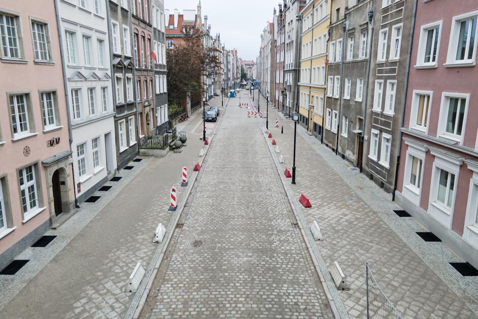 na zdjęciu brukowana ulica, nowo ułożone równe szare chodniki, wzdłuż nich kolorowe zabytkowe kamienice gdańskie
