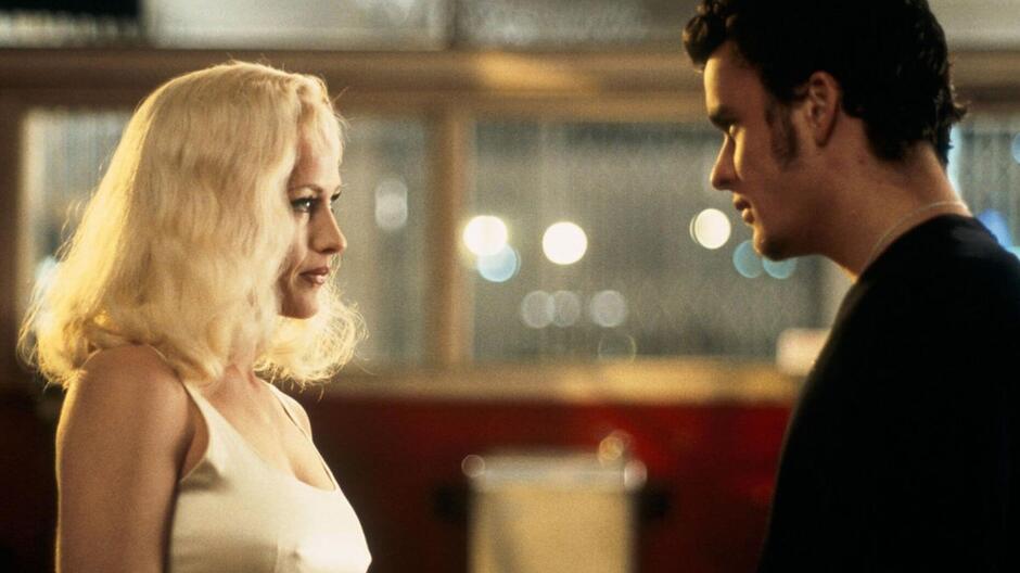 Kobieta z długimi blond włosami stoi naprzeciwko mężczyzny