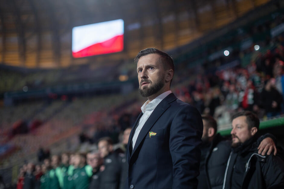 Mężczyzna w garniturze, za nim trybuny