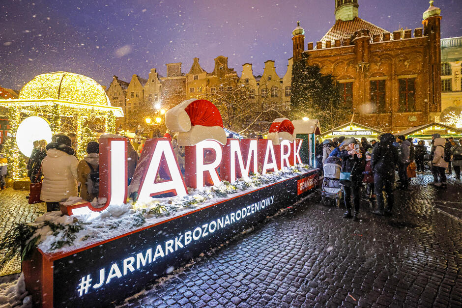 Świetlisty napis Jarmark Bożonarodzeniowy - w tle stoiska, choinki, ozdoby