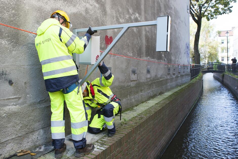 Dwóch mężczyzn montuje urządzenia do pomiaru poziomu wody w potoku