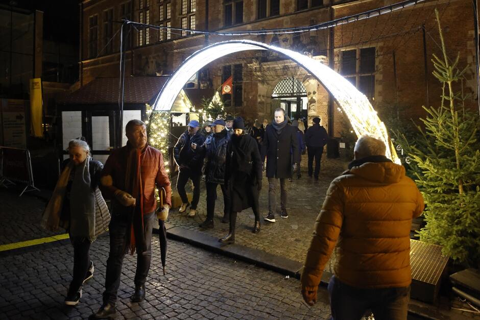 na zdjęciu iluminacja świetlna półkolista, przechodzą pod nią ludzie, w tle zabytkowy budynek