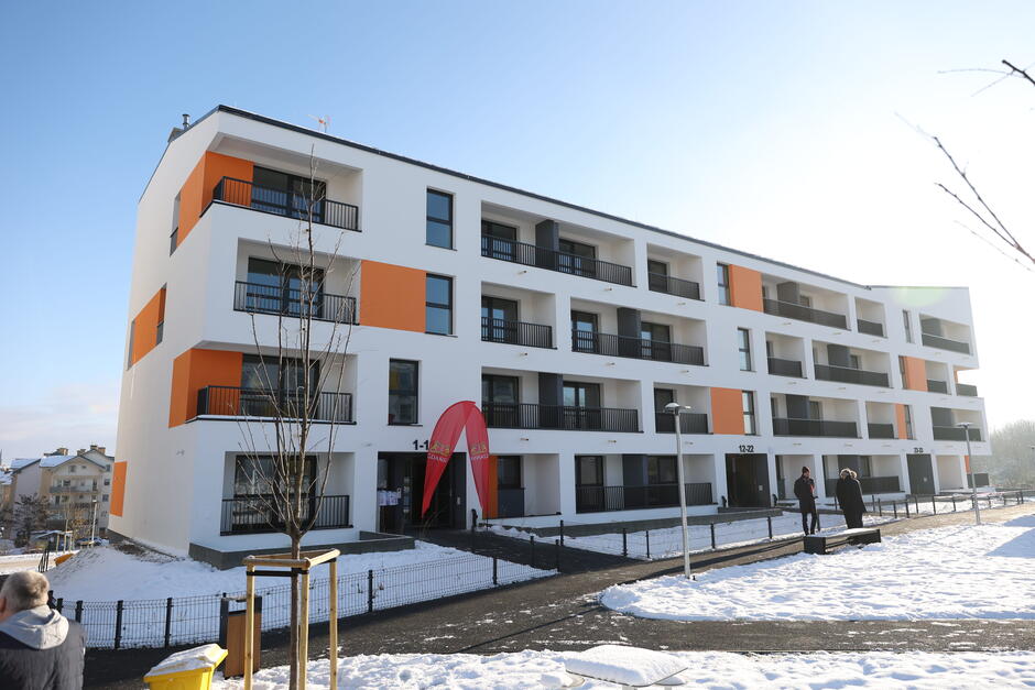 na zdjęciu czterokondygnacyjny budynek z oknami i balkonami, o elewacji biało - pomarańczowej
