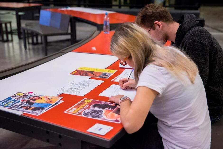 na zdjęciu dwie osoby, chłopak i dziewczyna, siedzą przy stoliku, piszą listy