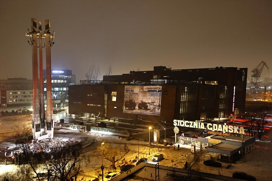 zdjęcie po zmroku, z drona, widać oświetlony masywny budynek europejskiego centrum solidarności, przed nim pomnik z trzech krzyży