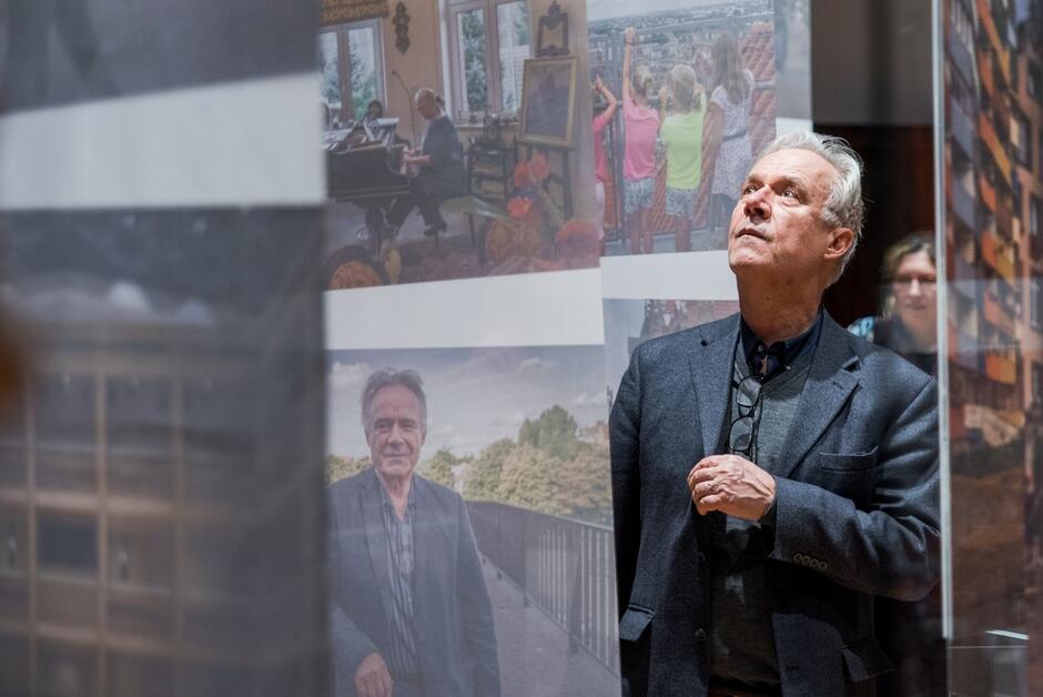 mężczyzna ogląda zdjęcia podwieszone do sufitu w galerii, patrzy w górę