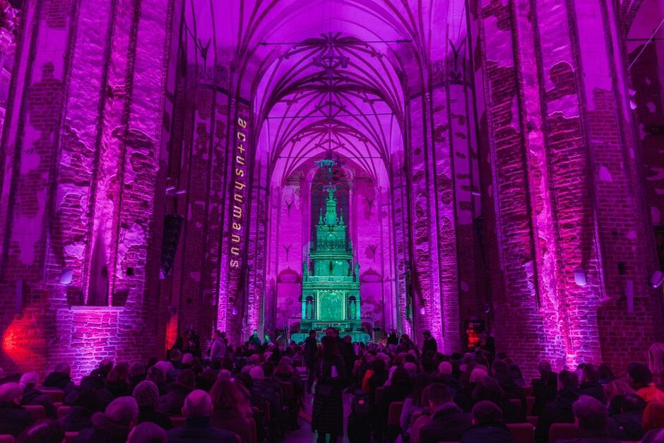 oświetlone na różowo wnętrze kościoła z cegły, w środku ludzie