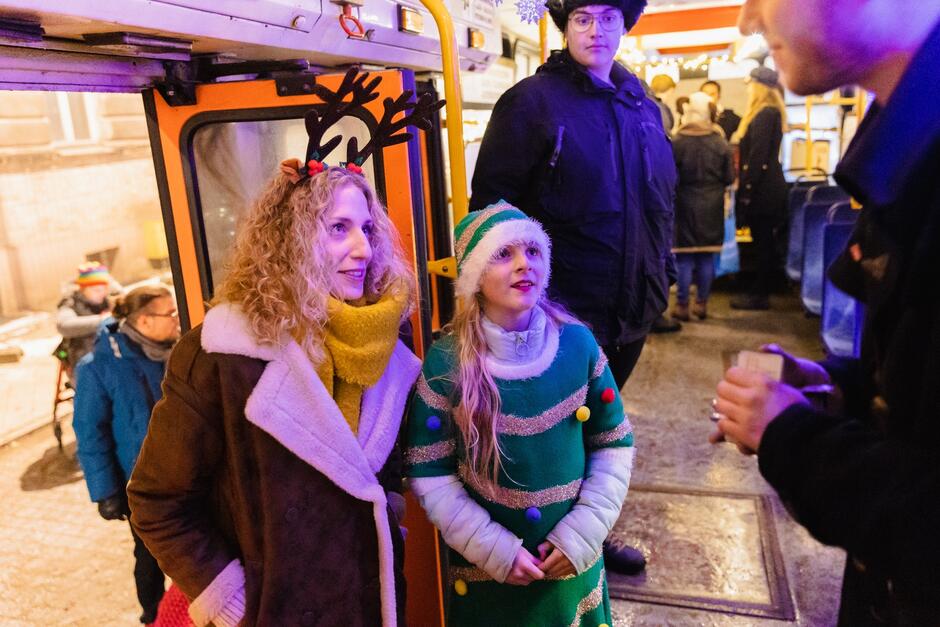 kobieta i około 7-letnia dziewczynka patrzą na widocznego częściowo młodego mężczyznę w mundurze konduktora tramwajowego