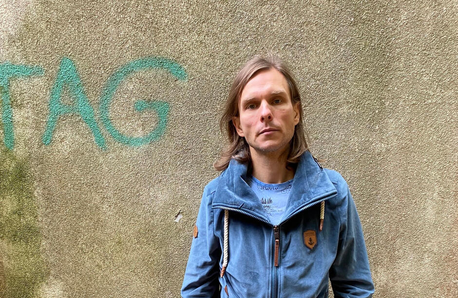 długowłosy szczupły mężczyzna na tle ściany z graffiti