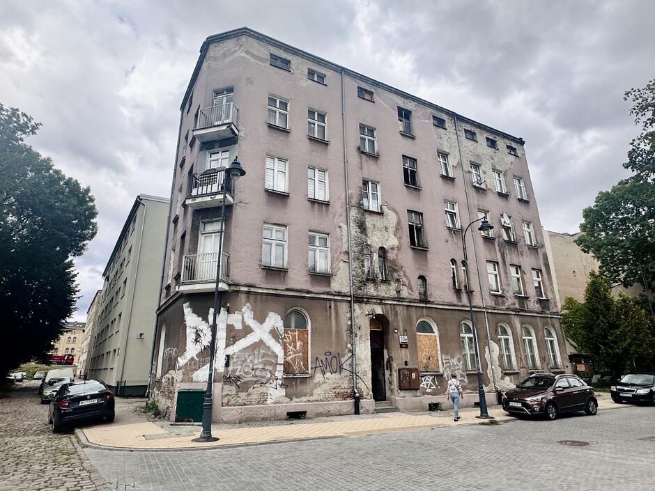 Na zdjęciu widać budynek z graffiti na ścianie. Budynek jest stary i zniszczony. Graffiti jest wykonane w różnych kolorach i przedstawia różne obrazy, takie jak postacie ludzkie, zwierzęta i symbole