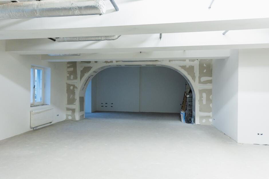 Na zdjęciu widać pusty pokój z dużą arkadą w środku. Pokój jest duży i jasny, z białymi ścianami i drewnianą podłogą. 