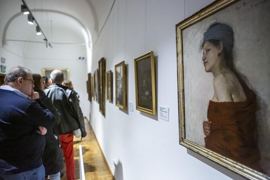 Galeria, ludzie przyglądają się obrazom powieszonym na ścianach