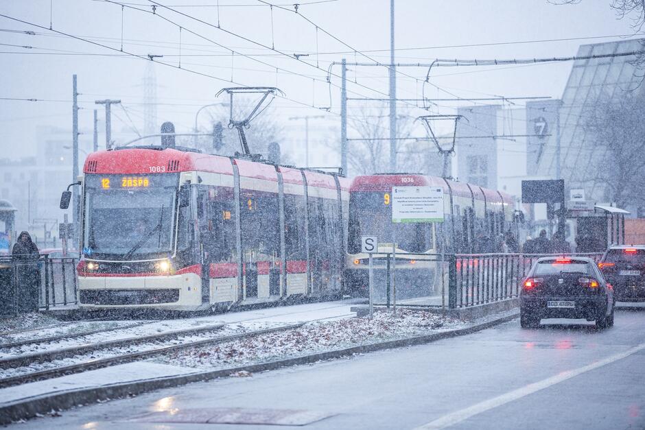 na zdjęciu dwa tramwaje kremowo czerwone, stoją przy przystanku, pada gęsty śnieg