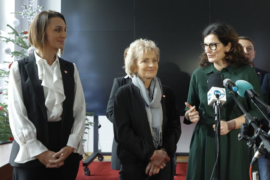 Trzy kobiety elegancko ubrane na konferencji prasowej 