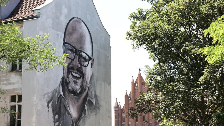 Mural na ścianie budynku przedstawiający uśmiechniętego mężczyznę w okularach