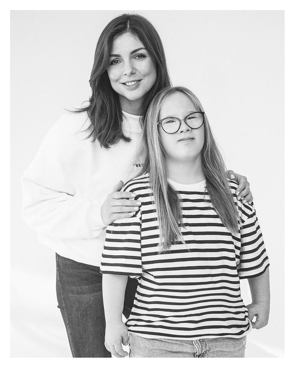 Czarno-białe zdjęcie: kobieta stoi obok dziewczyny z zespołem Downa, trzyma ją za ramię