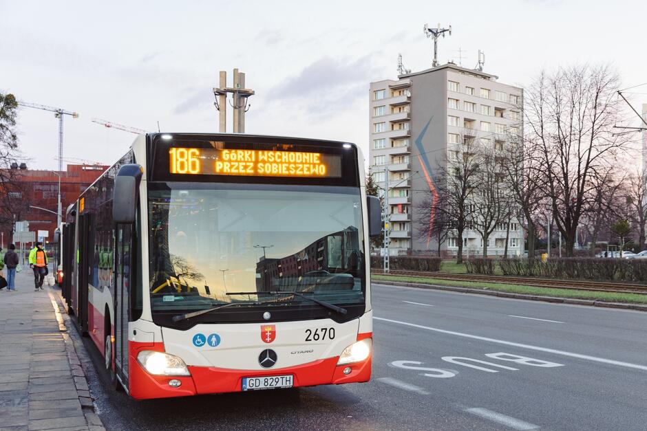 Autobus linii 186 odjeżdża z przystanku autobusowego. W tle jest widoczny pomnik Poległych Stoczniowców