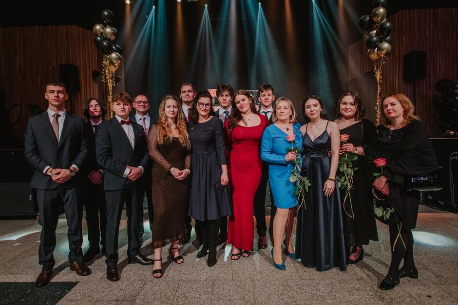 Kilkudziesięcioosobowa grupa elegancko ubranych młodych kobiet i mężczyzn pozuje na scenie do wspólnego zdjęcia, wśród nich jest prezydent Dulkiewicz 