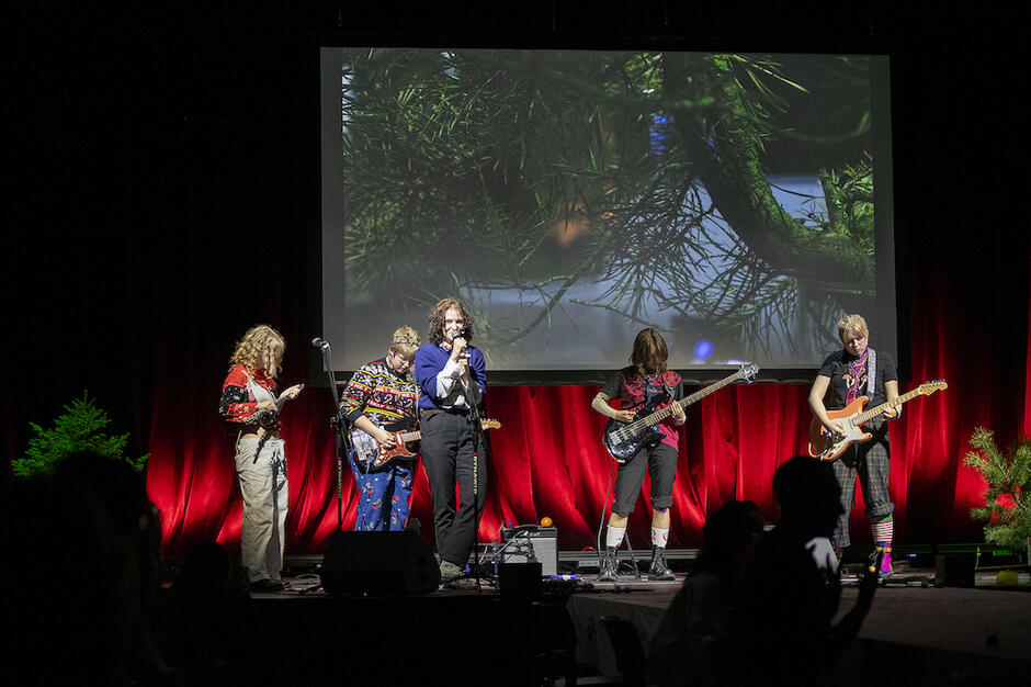 pięcioro młodych ludzi na scenie, grają na gitarach i śpiewają