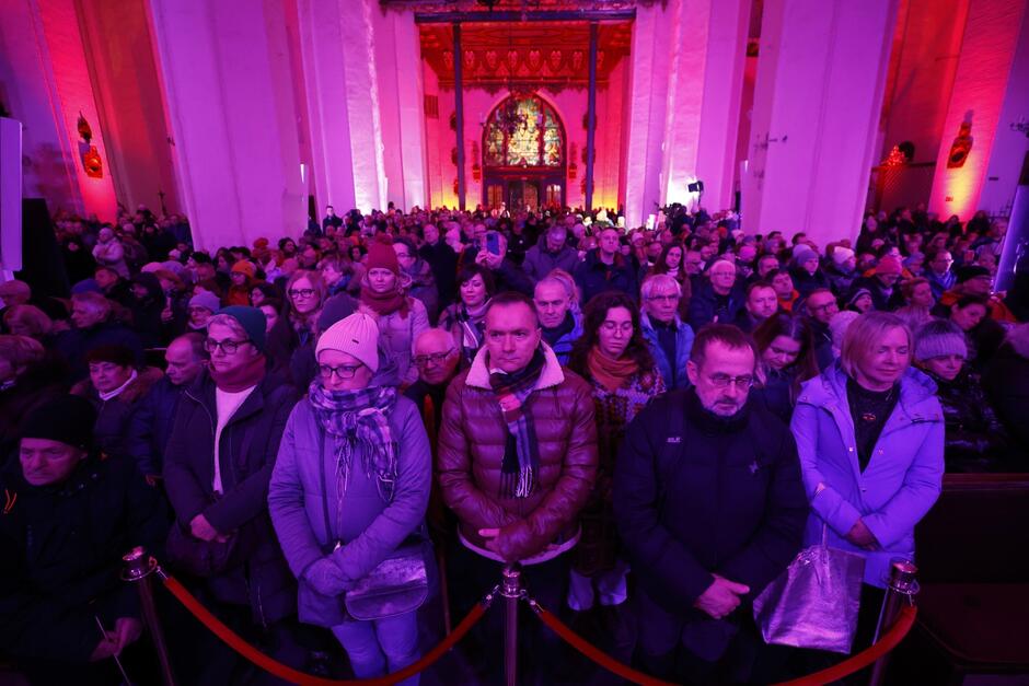 na zdjęciu setki osób stojących tłumnie w kościele, ściany świątyni podświetlone są na czerwono i fioletowo