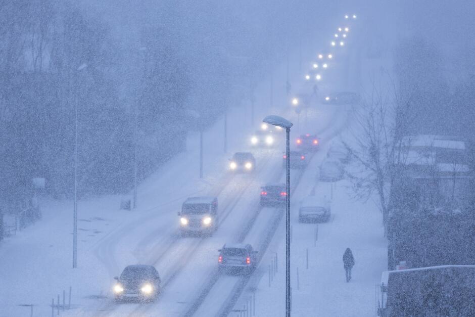 Gęsiego jadą samochody - wszystkie na zapalonych reflektorach, intensywnie sypie śniegiem