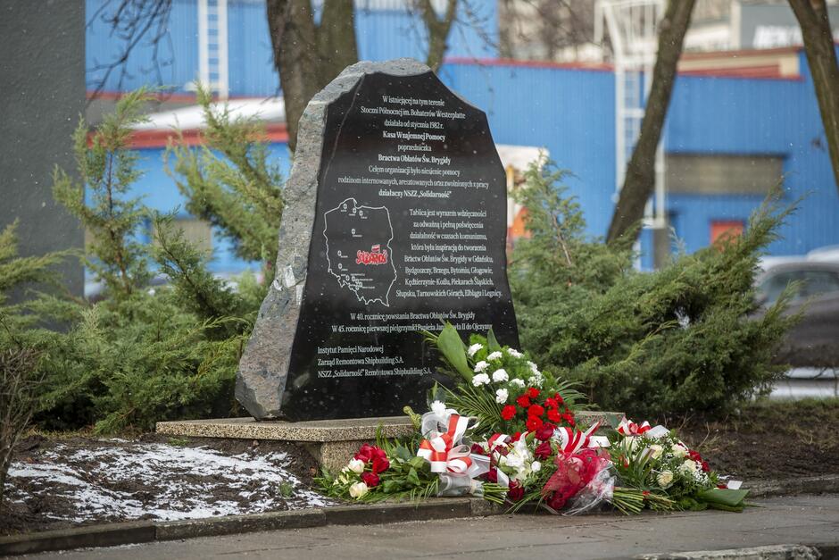 Czarna dużych rozmiarów bryła marmuru, zeszlifowana od strony frontowej - z napisami na temat Kasy Wzajemnej Pomocy i Bractwa Oblatów. Wokół kwiaty i wieńce z biało-czerwonymi wstążkami