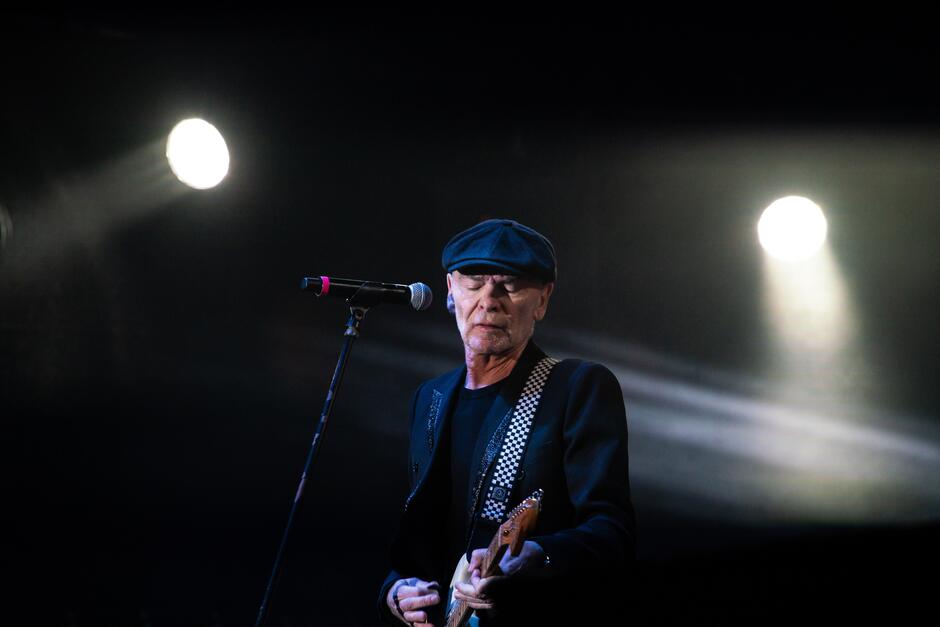 starszy mężczyzna z gitarą na scenie w świetle reflektorów