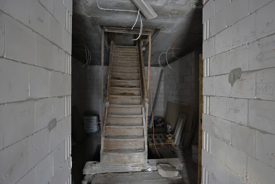 na zdjęciu zniszczone wąskie drewniane schody, widać wnętrze remontowanego budynku, są materiały budowlane wokół
