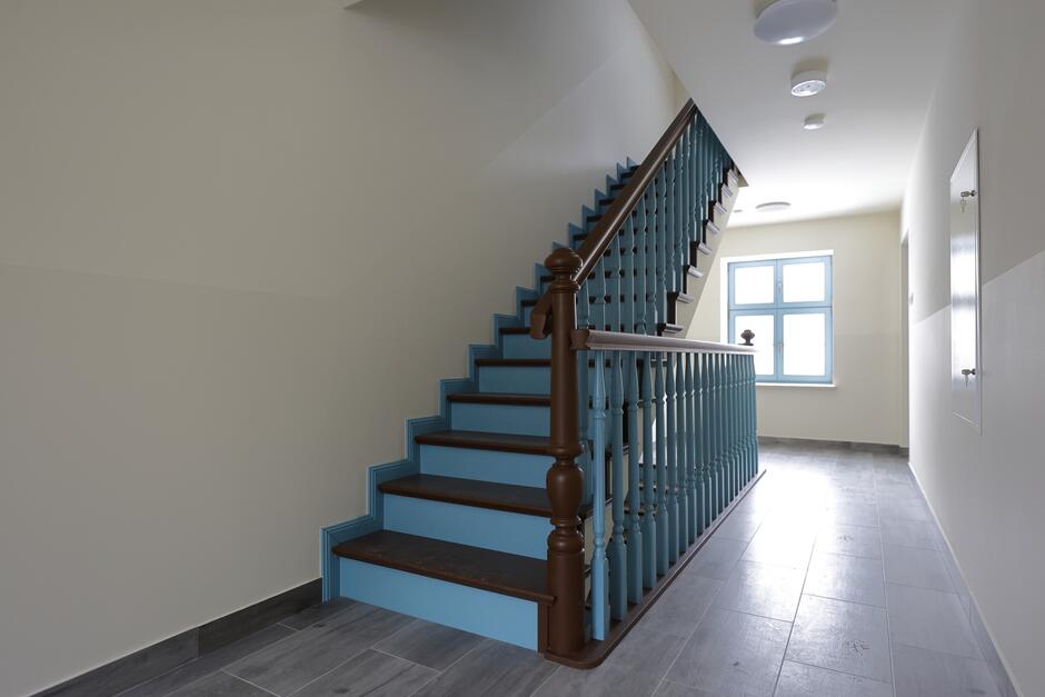 na zdjęciu klatka schodowa, i odnowione brązowo niebieskie schody z poręczą, widać też jasne ściany