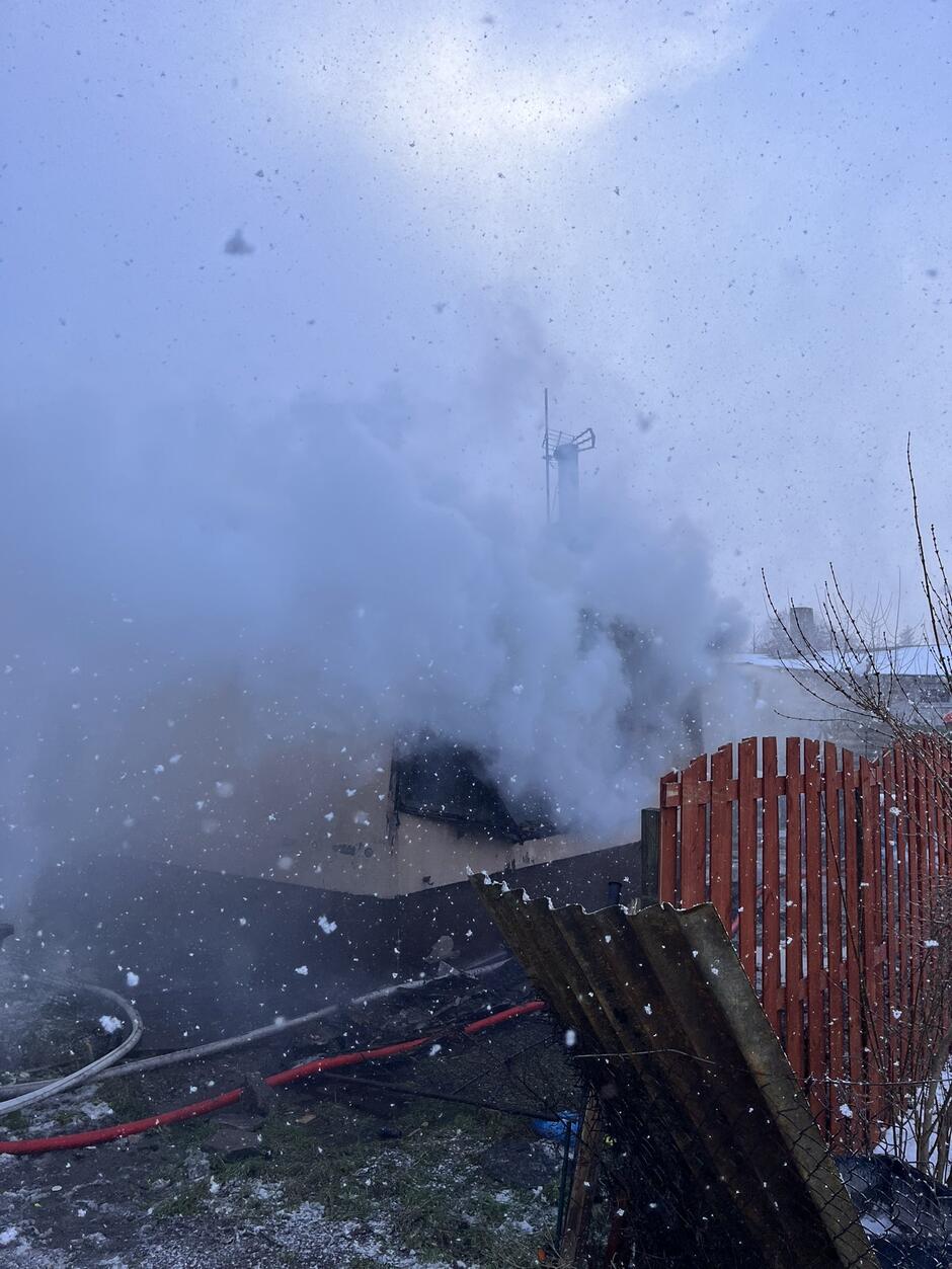 Połowa zdjęcia tonie w dymie, po prawej pomalowany na czerwono płot sztachetowy.