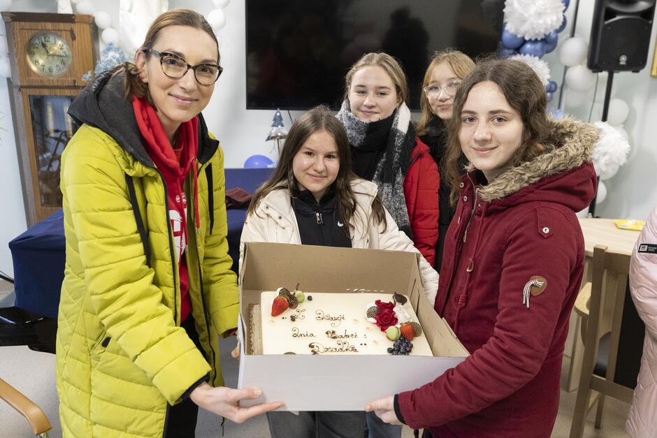 trzy dziewczyny i młoda kobieta trzymają pudło z tortem ozdobionym napisem z okazji dnia dziadka i babci