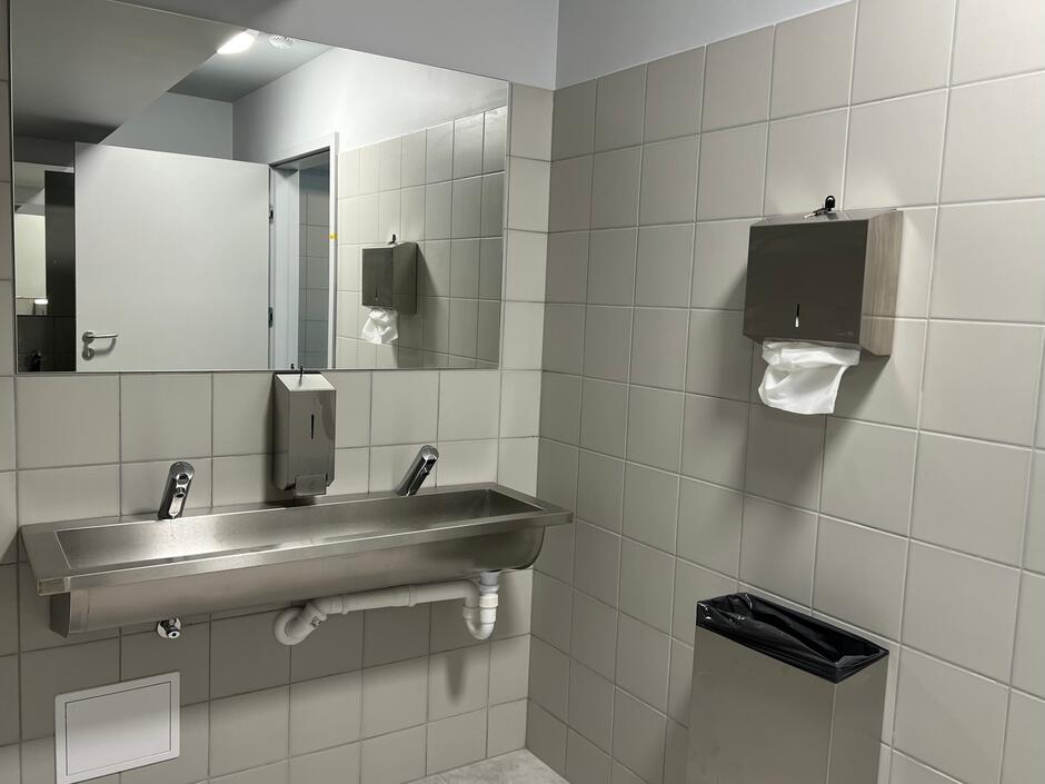 Wnętrze łazienki: na wprost umywalka, nad nią szafka z lustrem, po prawej na ścianie papierowe ręczniki