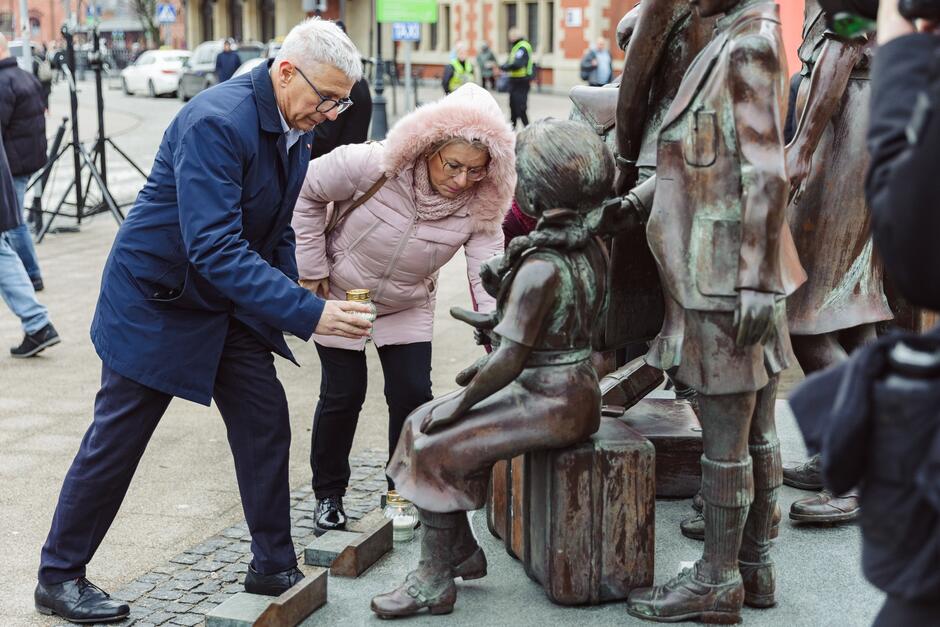 mężczyzna i kobieta zapalają znicz przy pomniku