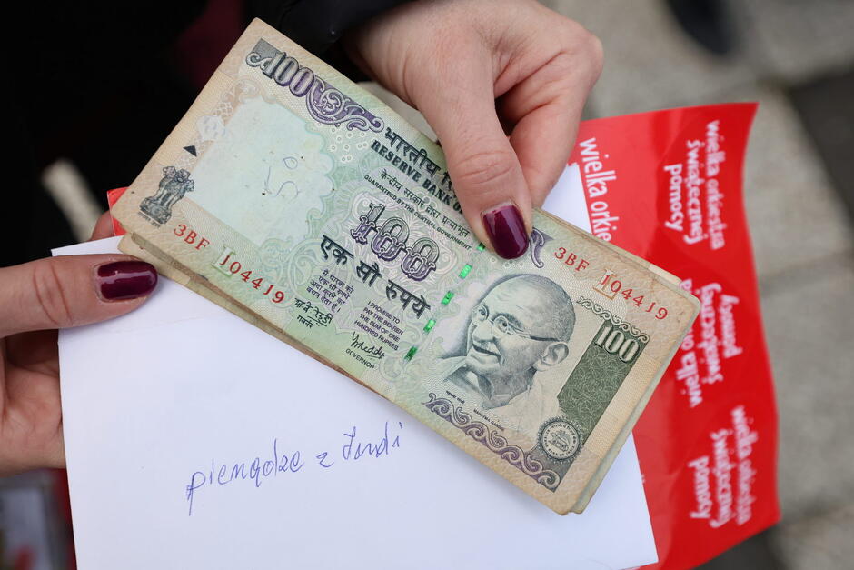 Pieniądz z wizerunkiem Gandhiego, pod nim kartka z napisem: pieniądze indyjskie