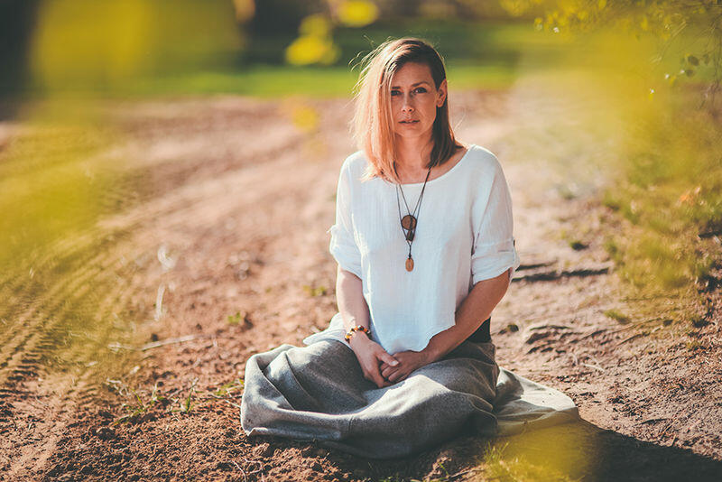 kobieta siedzi w siadzie skrzyżnym na drodze w otoczeniu zieleni