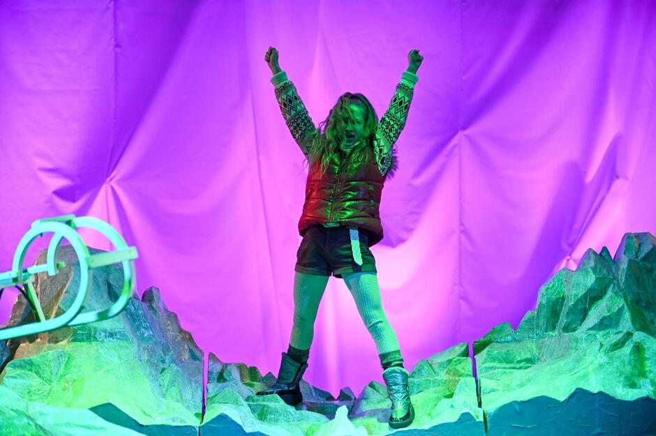 nieduża, szczupła aktora na scenie, przypominająca nastolatkę, stoi na scenie, ma obie ręce uniesione w górę