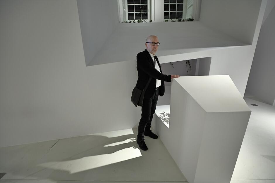 mężczyzna w okularach stoi w na klatce schodowej budynku przy schodach, całość jest pomalowana na biało