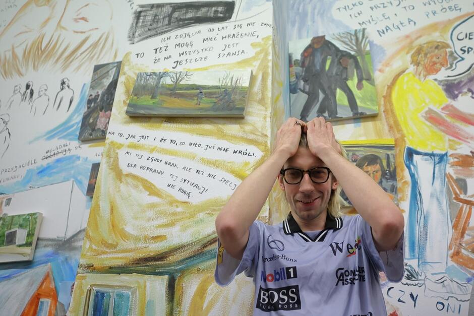Młody mężczyzna stoi na tle ściany pokrytej realistycznymi kolorowymi rysunkami
