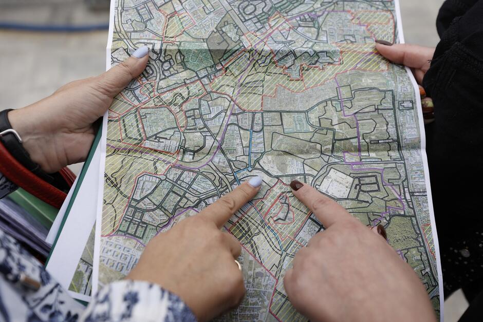 na zdjęciu dwie ludzie dłonie trzymające papierową mapę, obie dłonie wskazują konkretny punkt na mapie