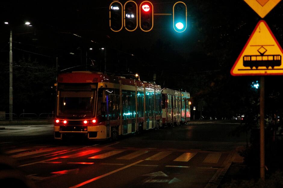 zdjęcie po zmroku, widać jadący po torach tramwaj w kolorach biało czerwonym