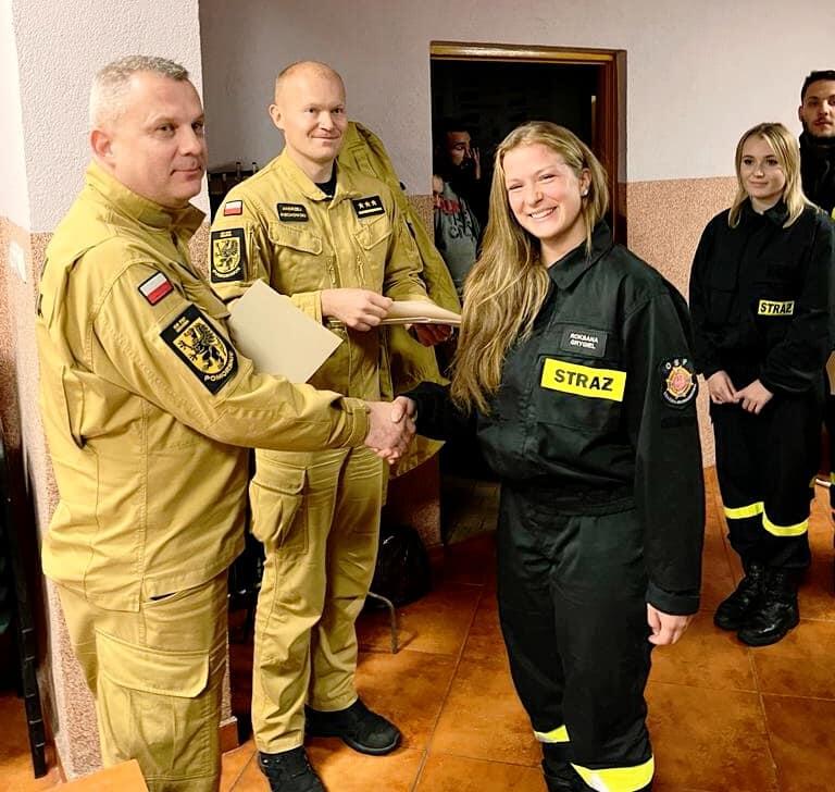 mężczyzna w mundurze strażaka wręcza dyplom kobiecie w mundurze strażaka