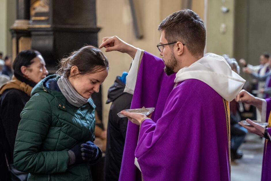 Ksiądz posypuje szczyptą popiołu głowę kobiety w kościele
