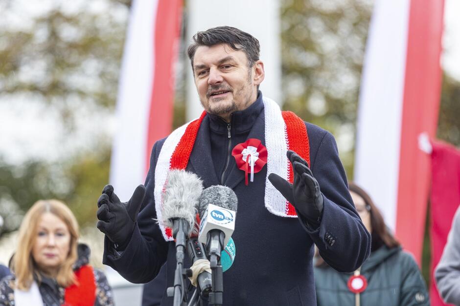 Mężczyzna w średni wieku przemawia w miejscu przystrojonym biało czerwonymi flagami - sam na na sobie biało-czerwony szalik