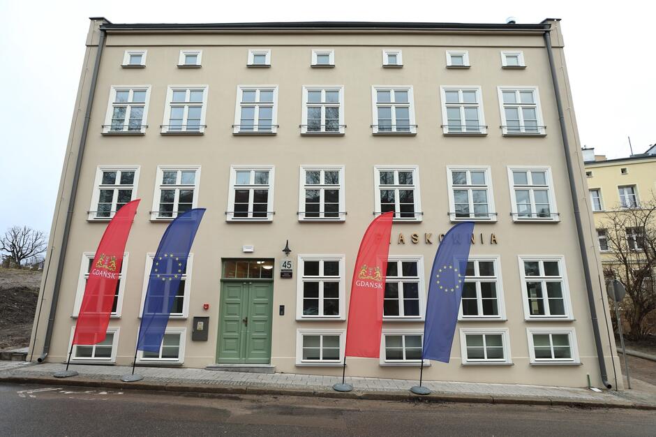 Budynek przy ul. Rogaczewskiego 45. Przez wejściem stoją flagi Gdańska i UE. 