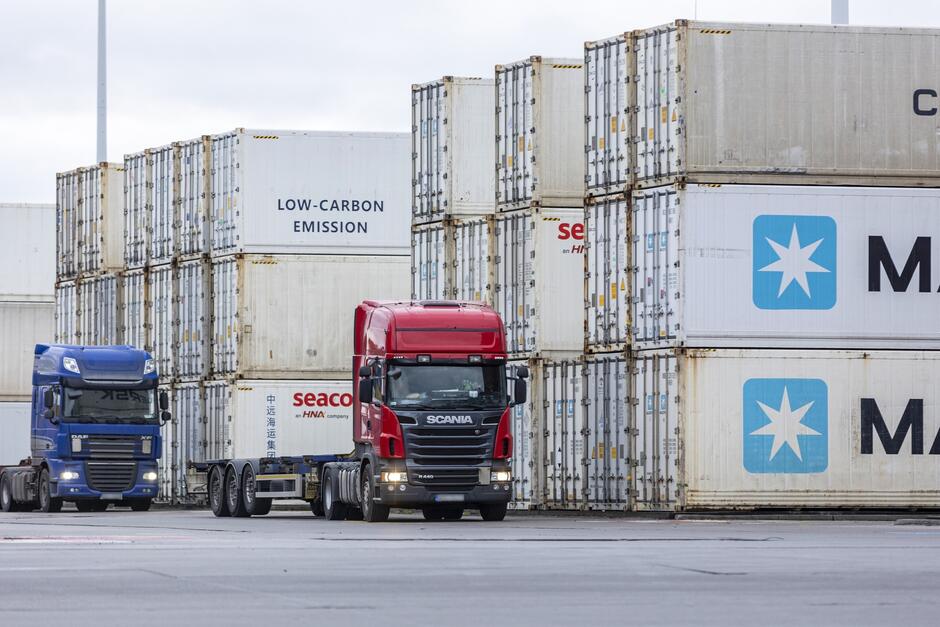 na zdjęciu dwie ciężarówki, a za nimi w tle kontenery transportowe