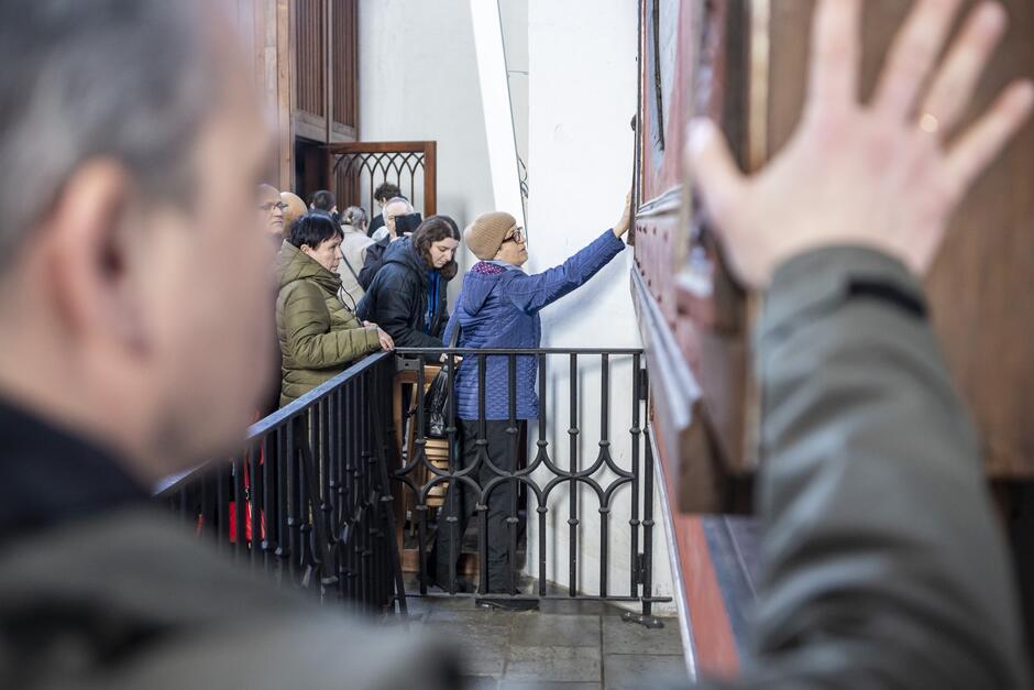 na zdjęciu osoby dotykają fragmentu drewnianego dużego zegara